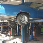 Blue classic car on lift in auto repair shop.